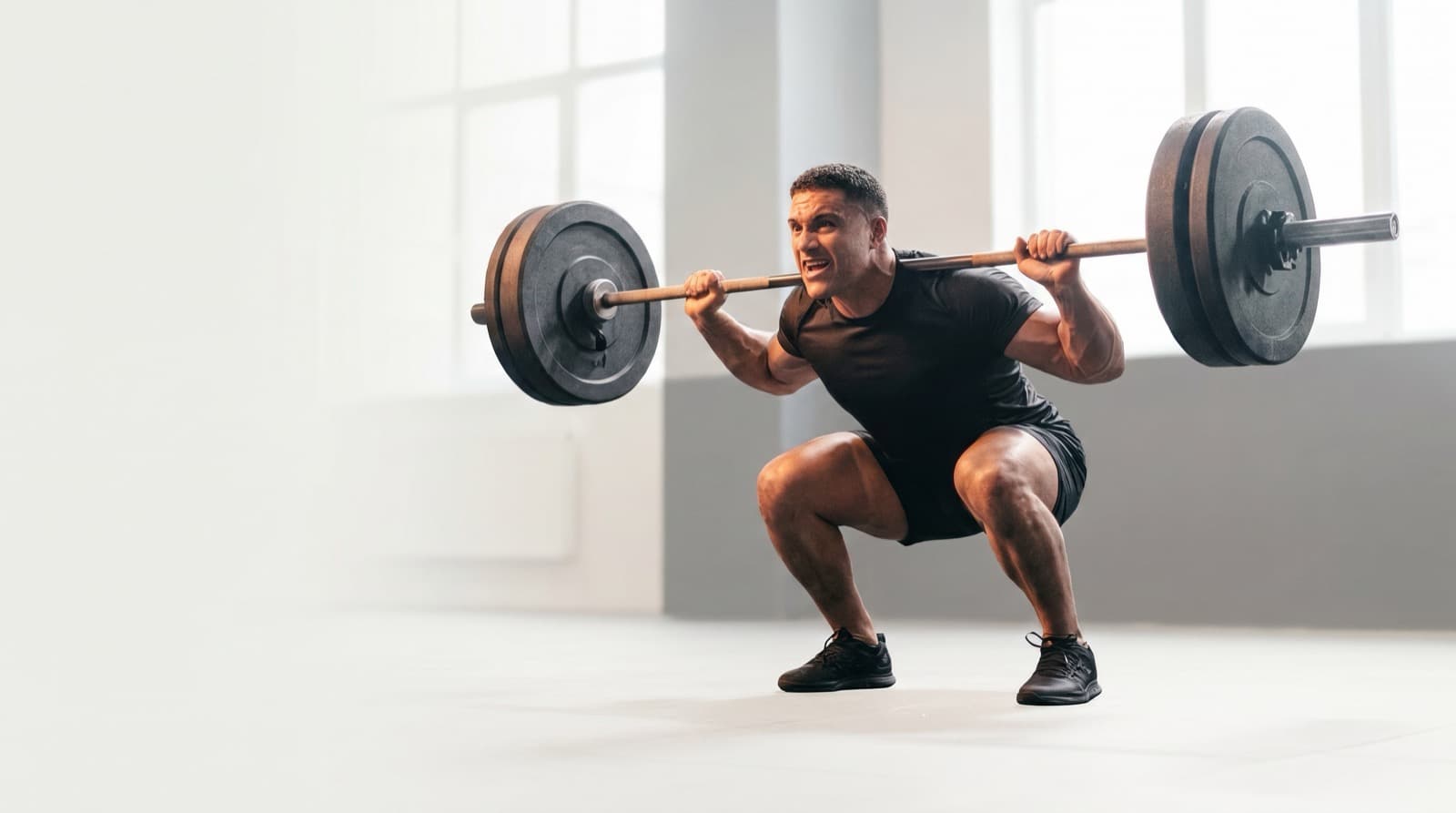 Atleta no fundo de um agachamento pesado com barra